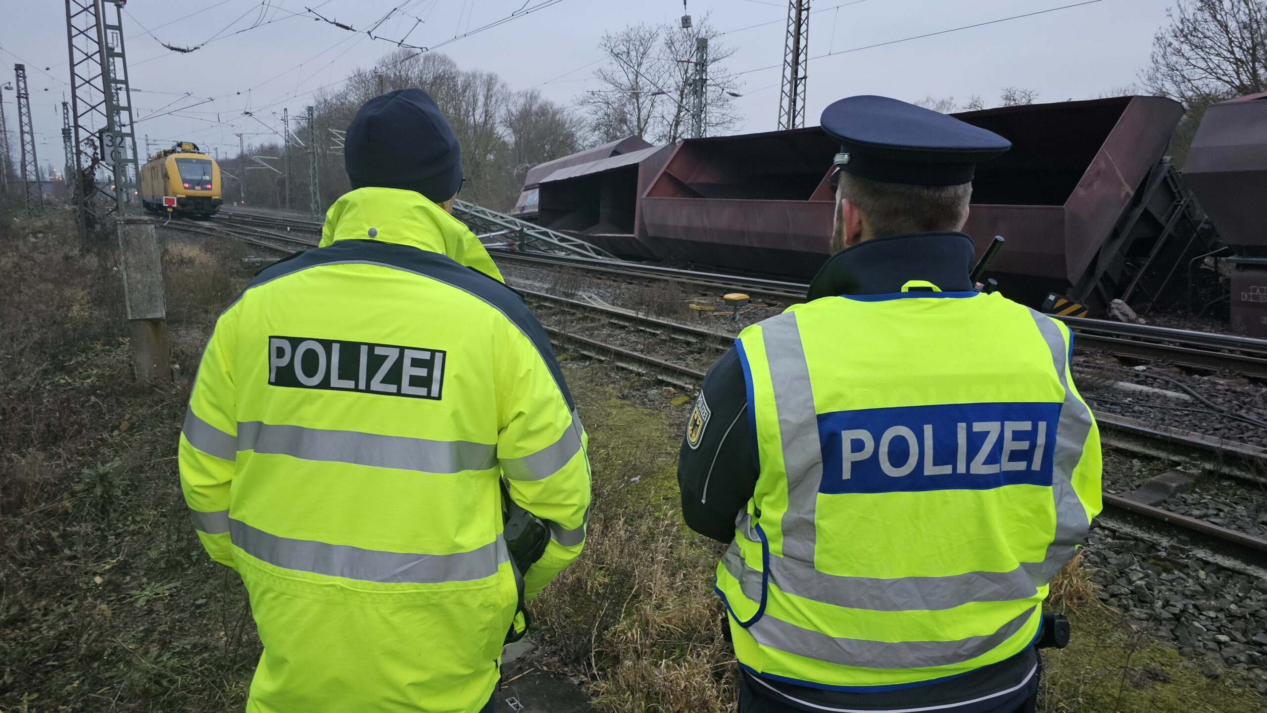 Einsatzkräfte der Bundespolizei stehen nach dem Zugunglück bei Elze an den Gleisen neben umgekippten Schüttgutwagen.