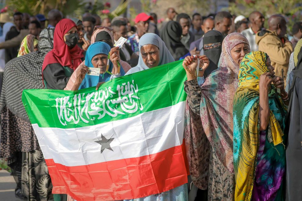 Eine Frau zeigt die somaliländische Flagge, während die Menschen vor einem Wahllokal Schlange stehen, um ihre Stimme bei den somaliländischen Präsidentschaftswahlen 2024 abzugeben.