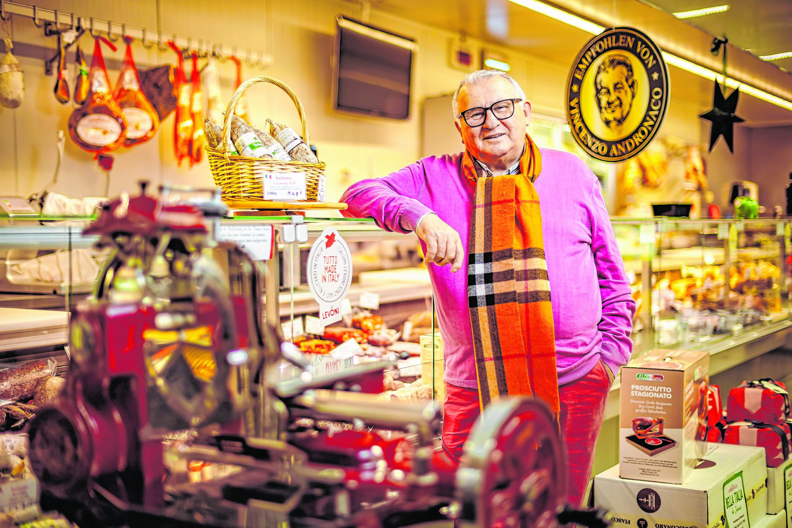 Mann mit buntem Schal lehnt an einer Wursttheke