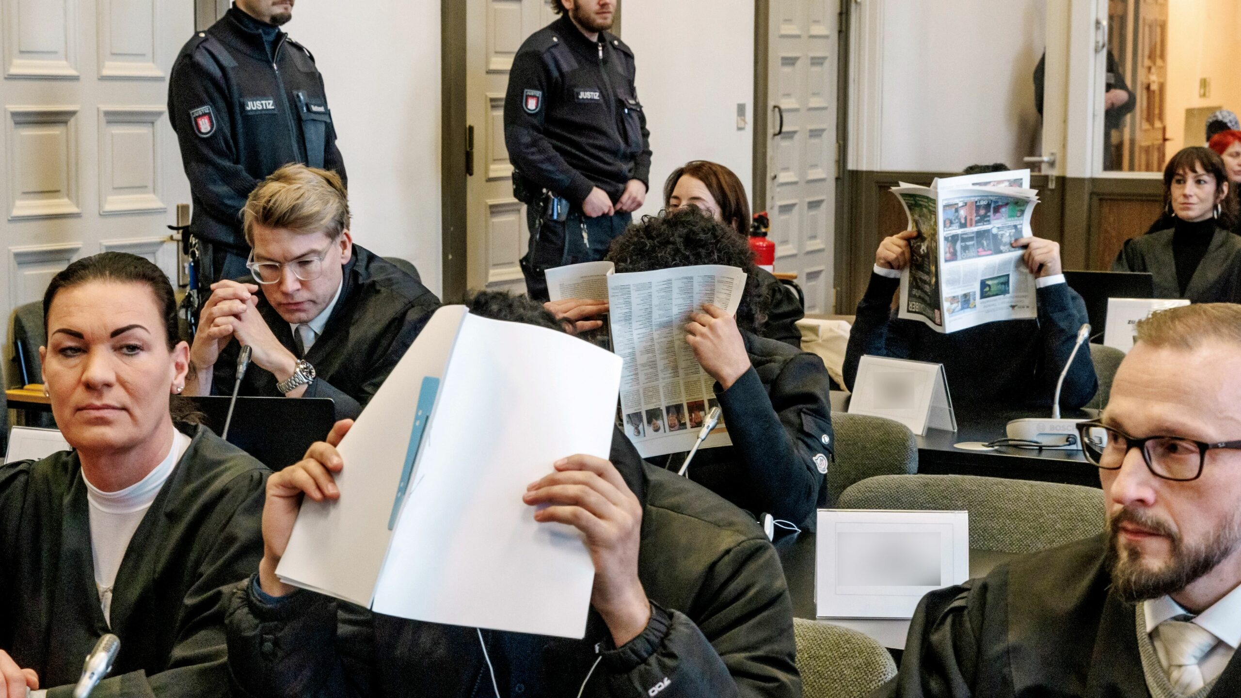 Die Angeklagten verbergen im Gerichtssaal ihre Gesichter.