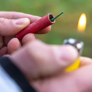 Ein einzelner Böller wird direkt in der Hand mit einem Feuerzeug entzündet.