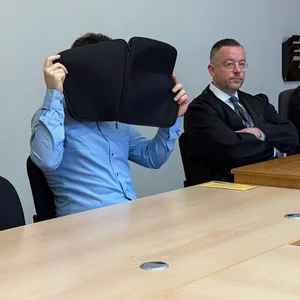 Der Angeklagte Patrick G. sitzt neben seinem Verteidiger und hält sich eine Laptop-Hülle vor sein Gesicht.