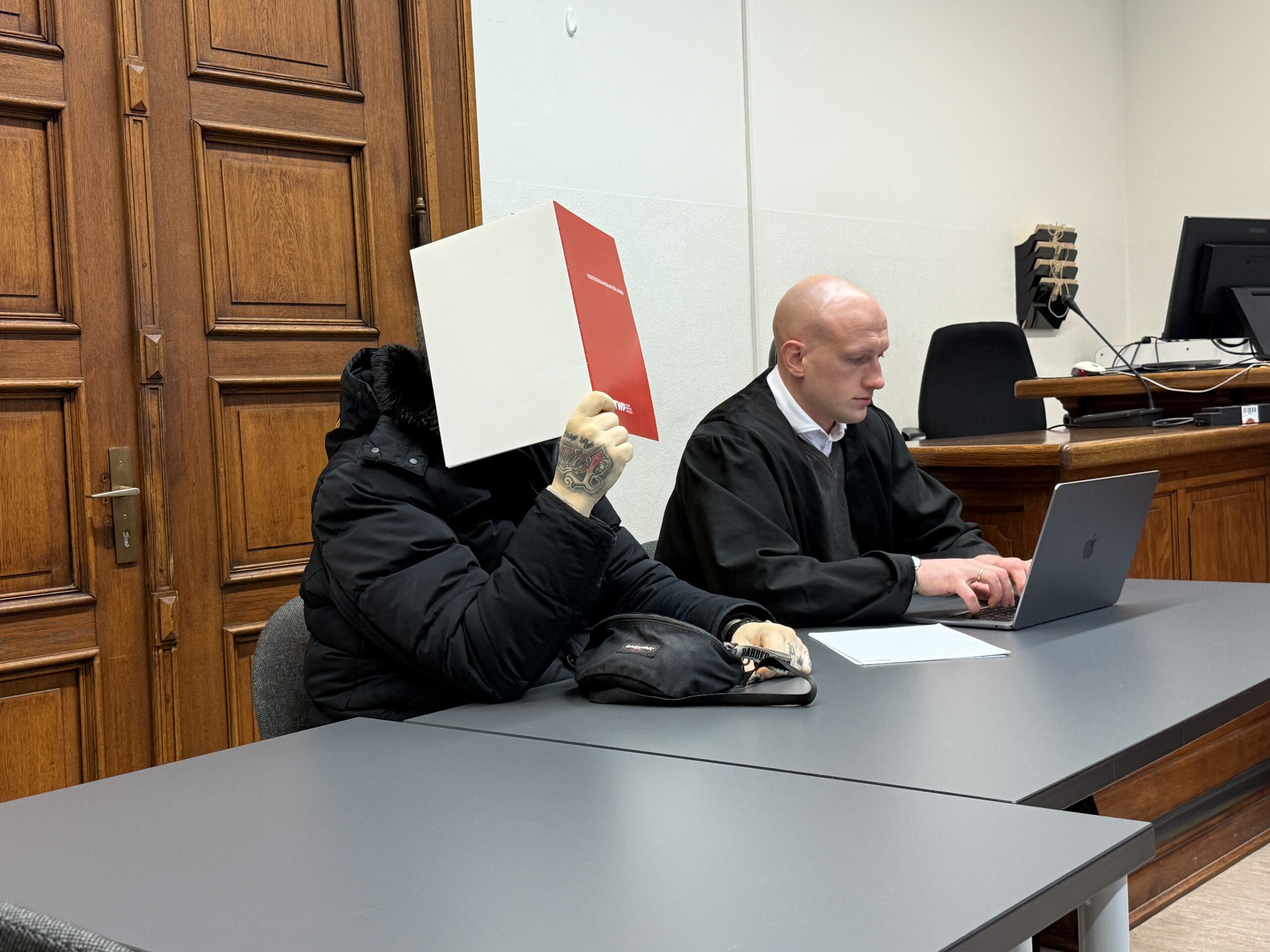 Der Angeklagte Patrik D. sitzt mit einer Mappe vor dem Gesicht neben seinem Verteidiger