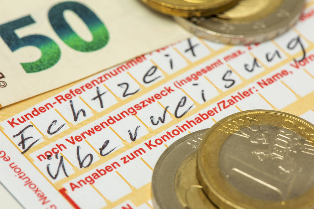 Ein Überweisungsformular mit Geldstücken und Geldscheinen (Symbolfoto)