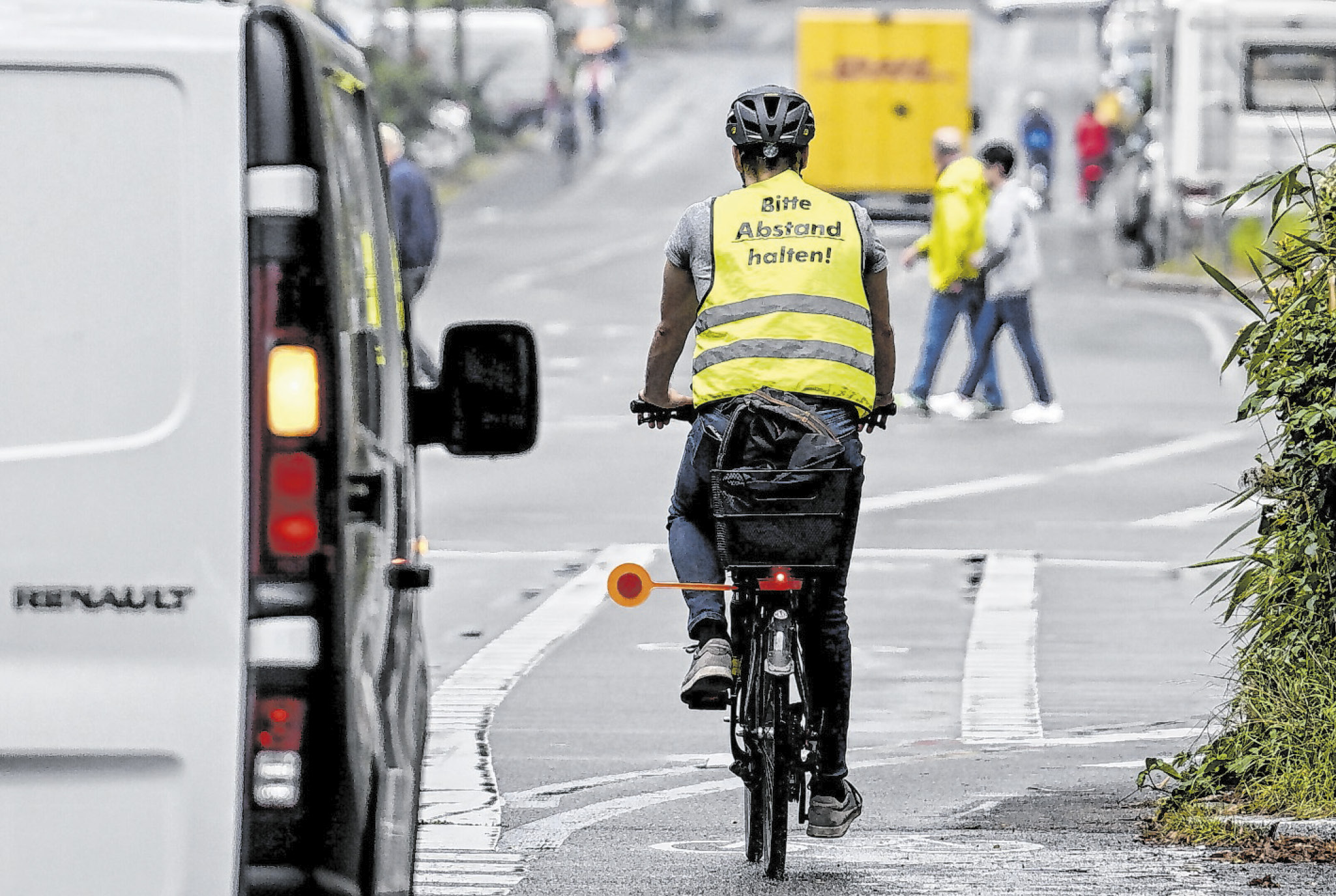 Eine Person auf einem Fahrrad trägt eine gelbe Warnweste auf der „Abstand halten!“ steht.