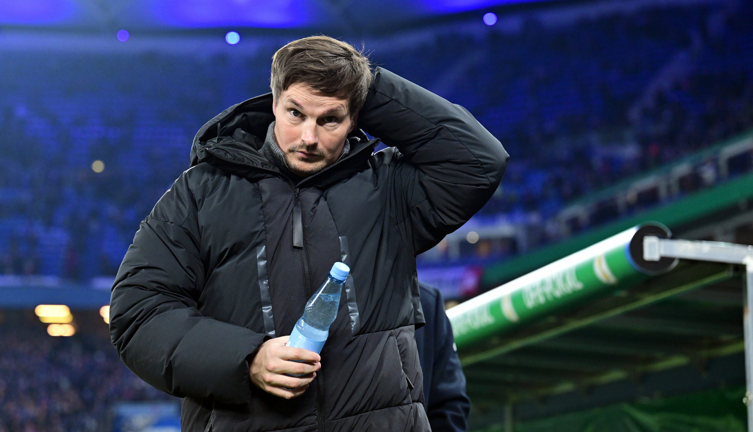 HSV-Trainer Merlin Polzin hat eine Wasserfalsche in der Hand und fasst sich mit der anderen an den Hinterkopf.