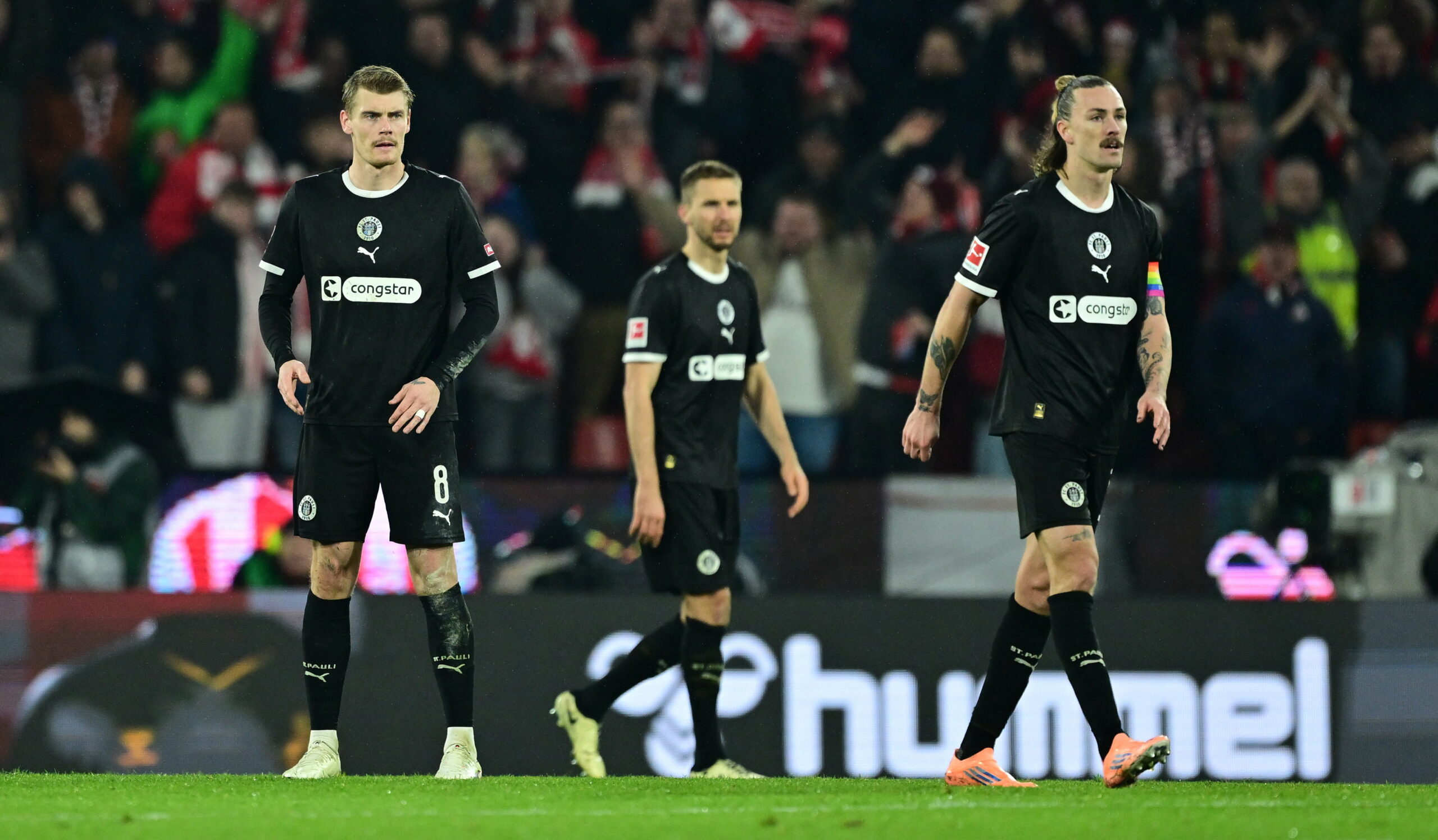 Eric Smith, Karol Mets und Jackson Irvine stehen während des Spiels in Köln auf dem Rasen