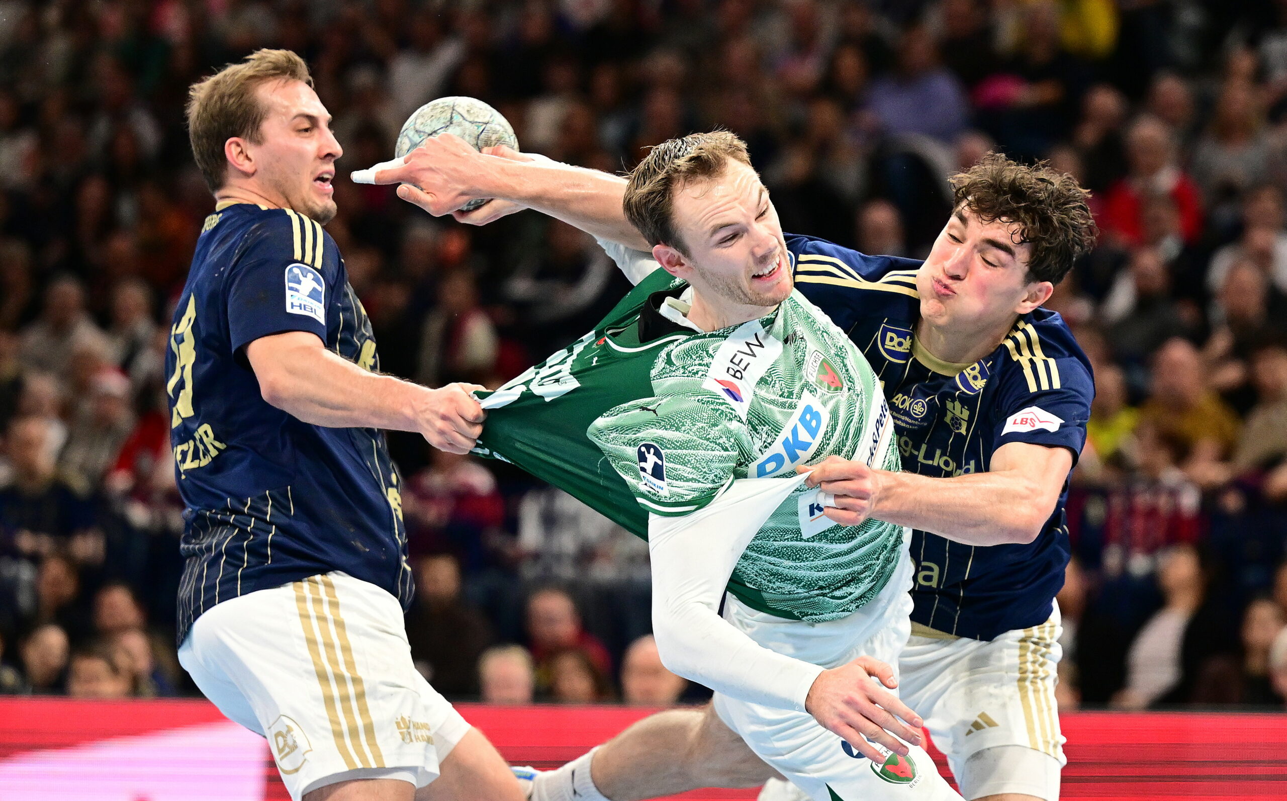 Mathias Gidsel wirft auf das Tor und wird von zwei Hamburger Gegenspielern bedrängt