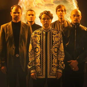 Fünf Männer stehen vor einer im Hintergrund angedeuteten Feuerkugel, vier tragen schwarze Kleidung, in der Mitte steht Christian Friedel in einem gemusterten Oberteil.