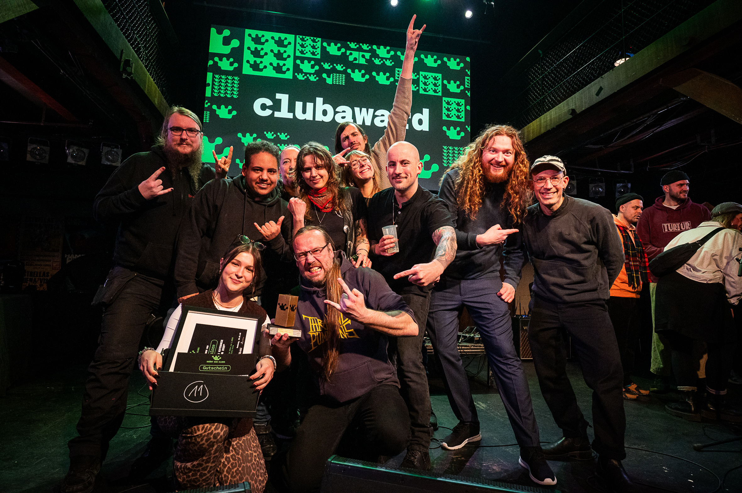 Viele lächelnde und lachende Menschen auf der Bühne, im Hintergrund steht auf einer Leinwand