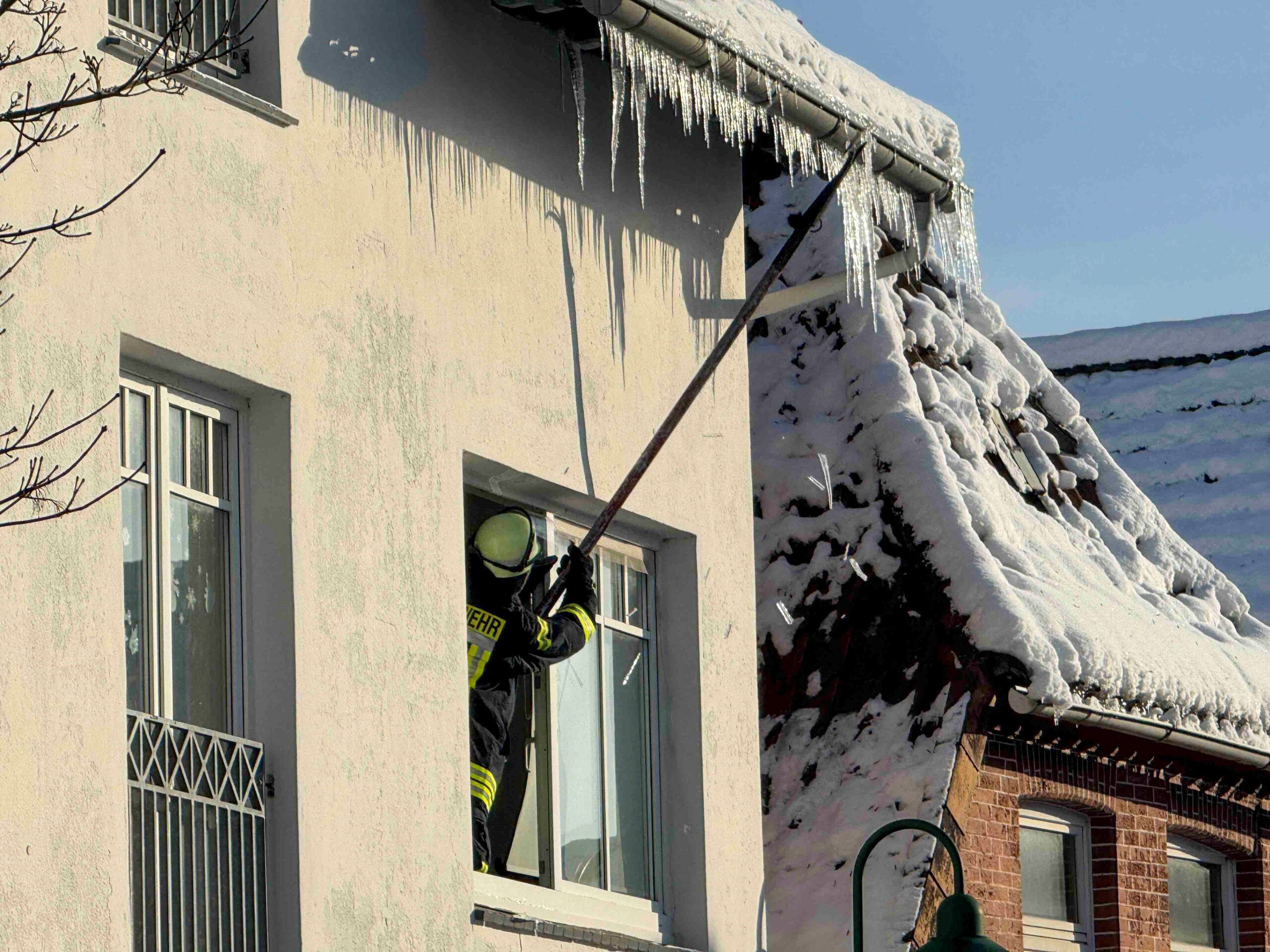 Ein Feuerwehrmann schlägt gefährliche Eiszapfen von einem Dach in Horneburg bei Hamburg ab.