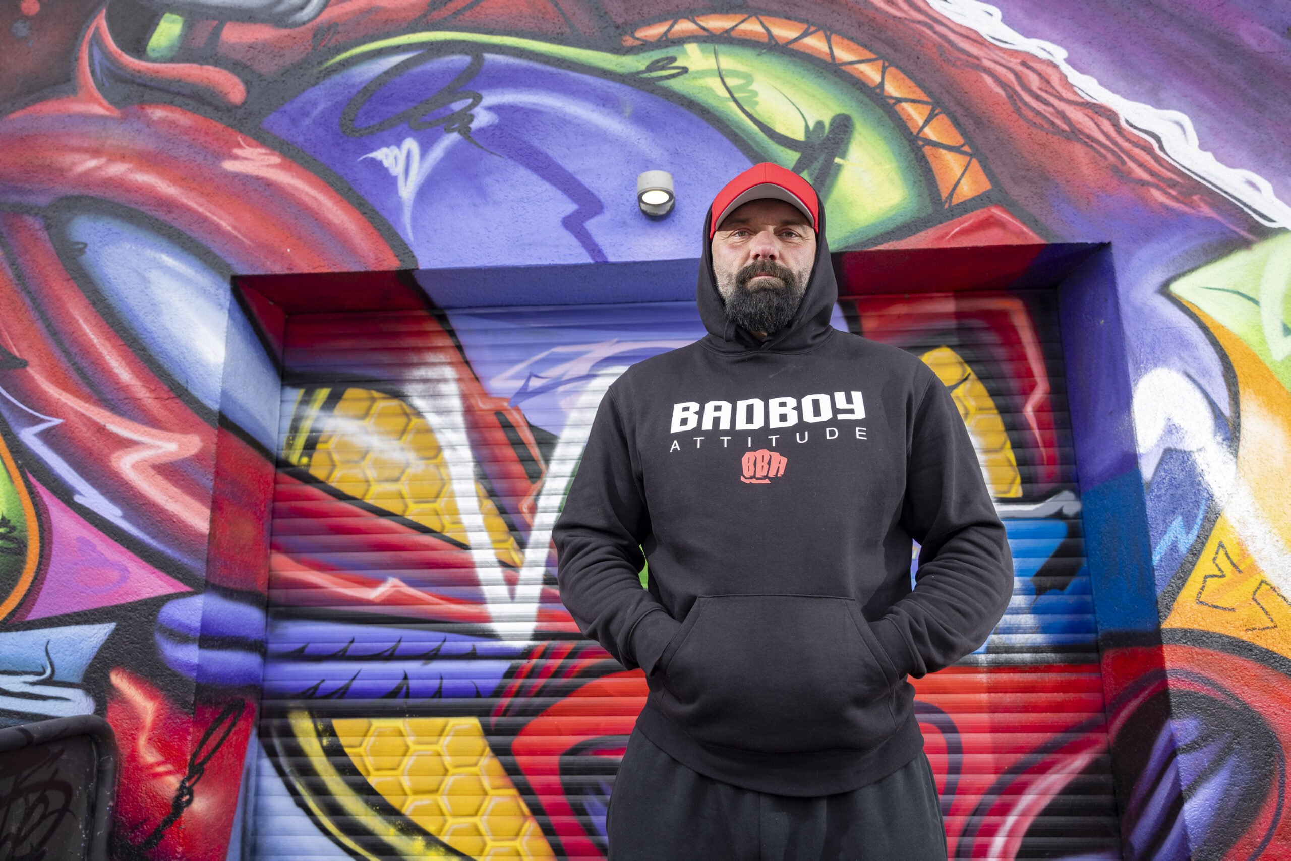 Jan Schütt steht auf dem Kiez vor einer Wand mit Graffiti