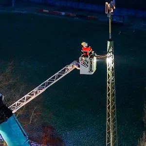 Eine Person ist auf einem Kran, der zum Sirenenmast reicht.