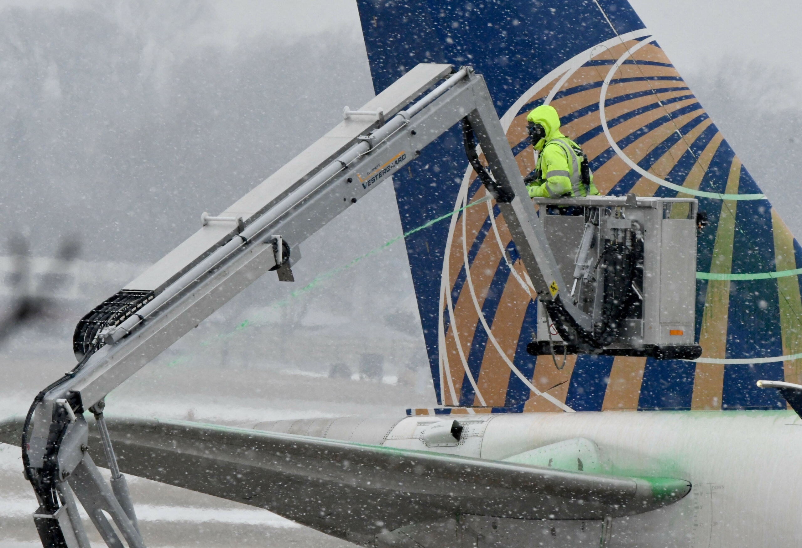 Eine Person steht bei Schneewetter auf einem Kran, an einem Flugzeug.