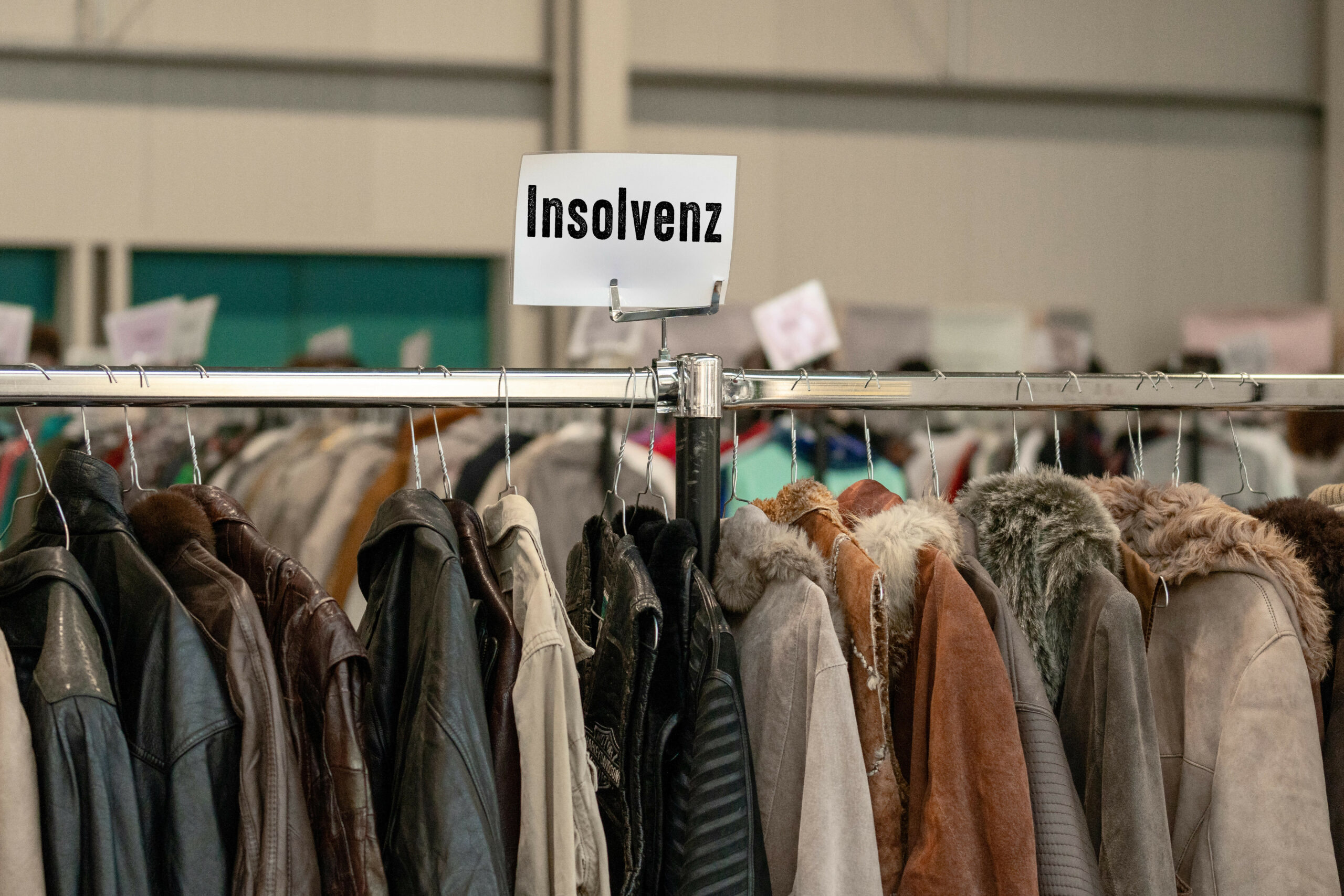 Jacken hängen auf einem Kleiderständer. Darüber das Schild „Insolvenz“