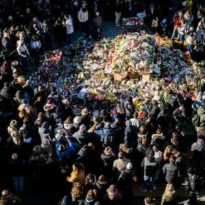 Eine große Gruppe an Menschen versammelte sich um eine Gedenkstätte mit Blumen und Kerzen.