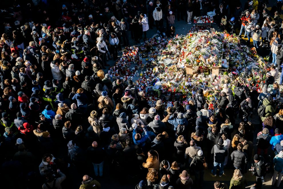Eine große Gruppe an Menschen versammelte sich um eine Gedenkstätte mit Blumen und Kerzen.