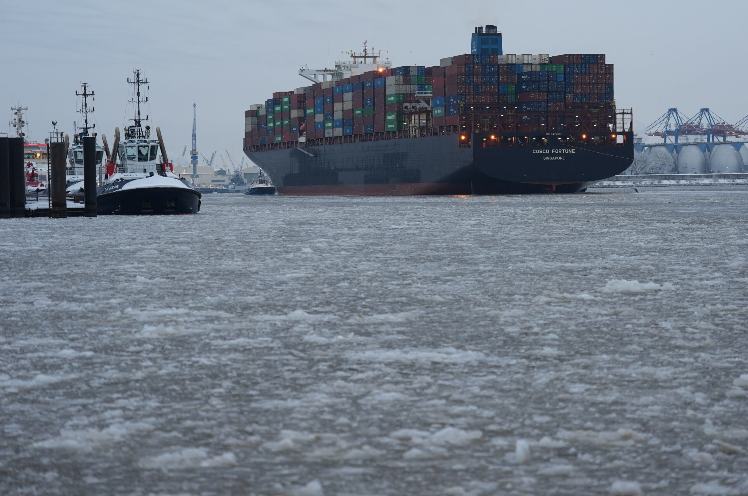 Ein Containerschiff fährt auf der mit Eisschollen bedeckten Elbe in den Hafen ein.