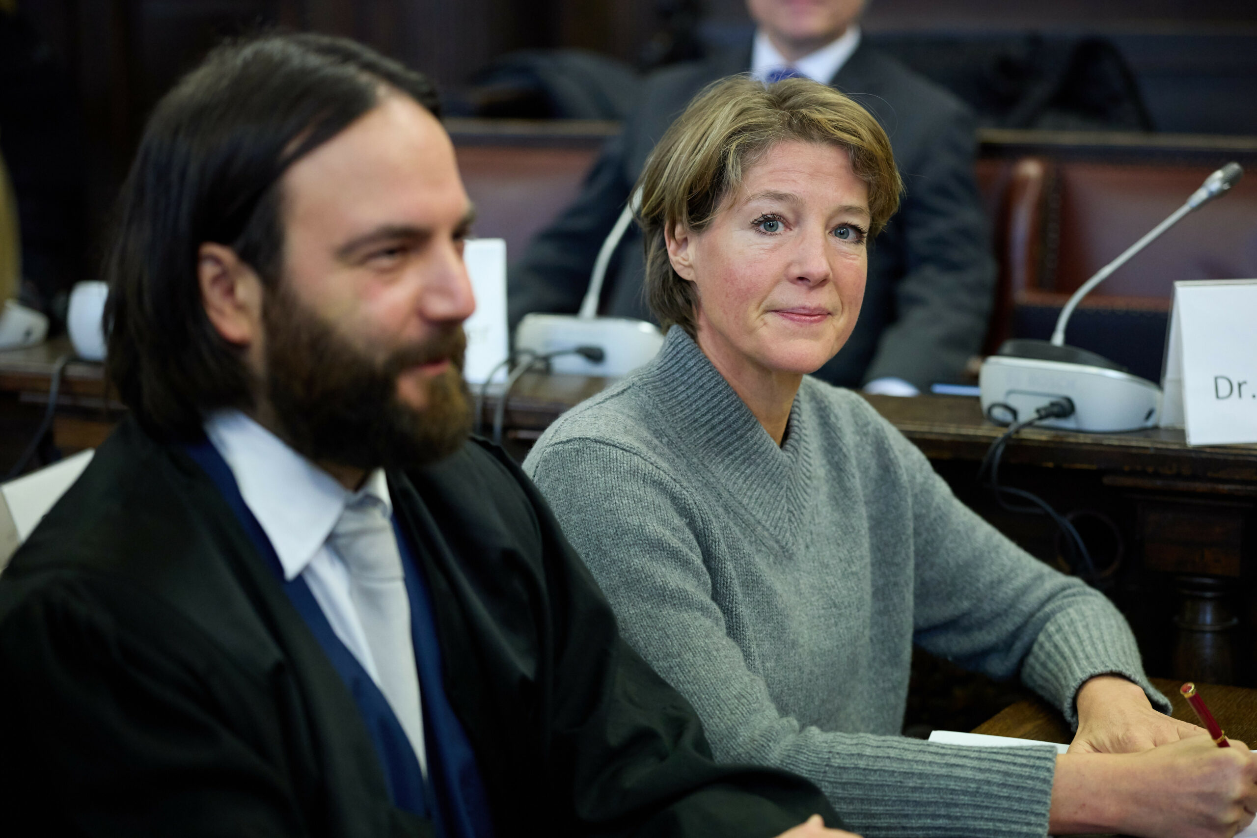 Frau mit kurzen Haaren und grauem Pulli neben Mann in Robe