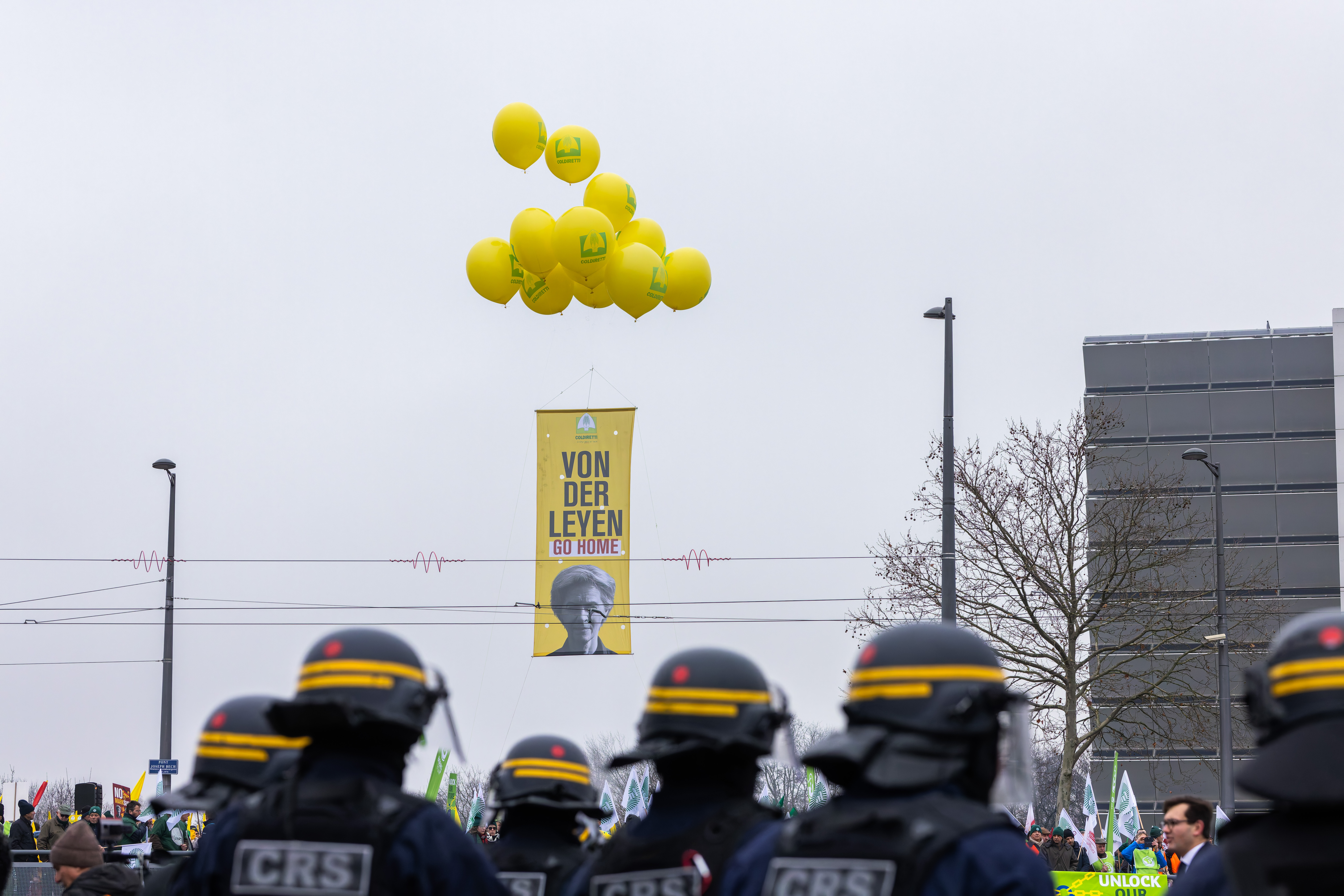 Ein Plakat mit der Aufschrift «von der Leyen go home» hängt an Heliumballons während im Vordergrund französische Polizisten zu sehen sind.