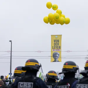Ein Plakat mit der Aufschrift «von der Leyen go home» hängt an Heliumballons während im Vordergrund französische Polizisten zu sehen sind.