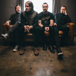 Die vier Mitglieder von Alter Bridge sitzen nebeneinander auf einem Sofa.