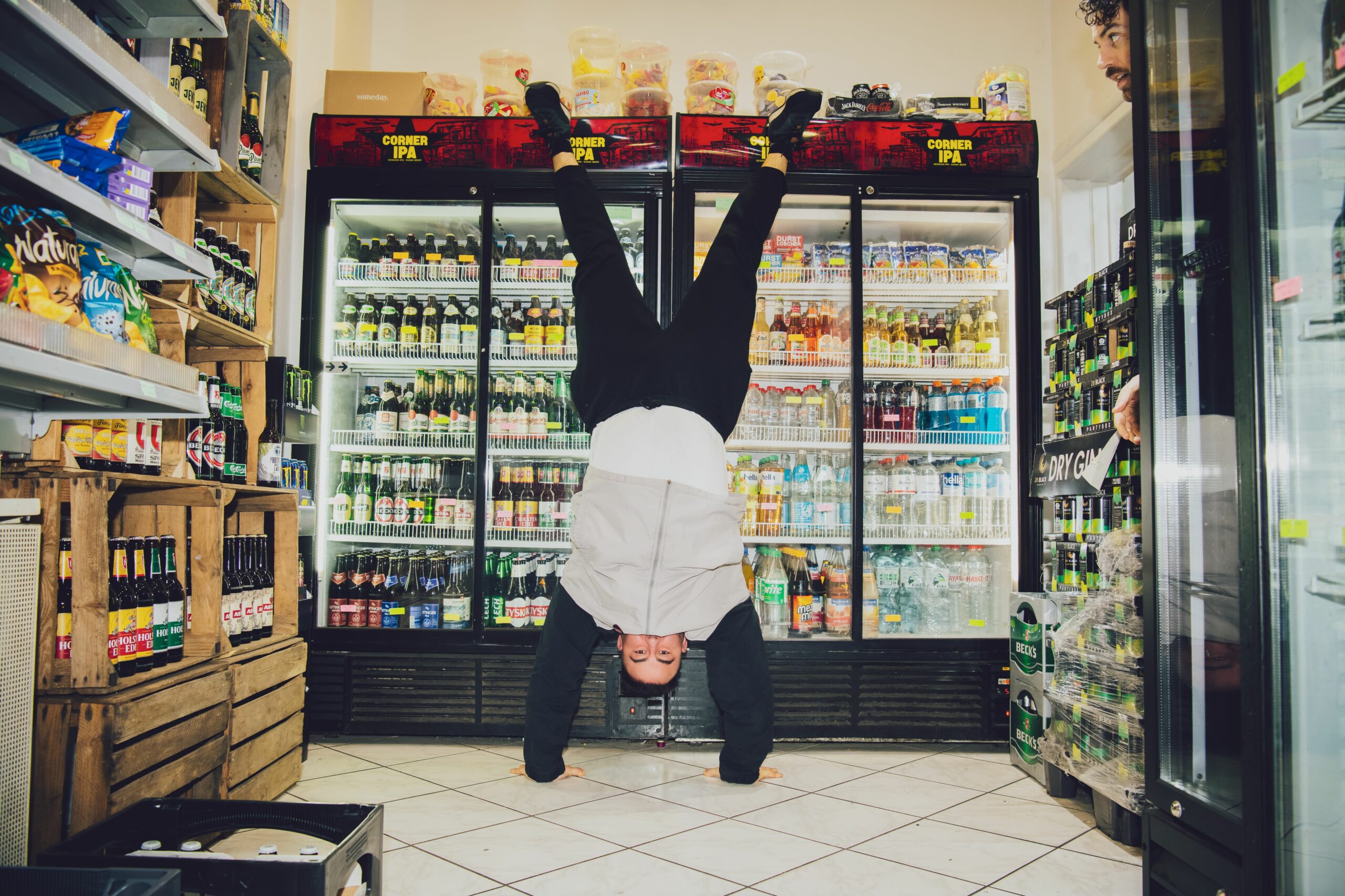 Ein Mann macht einen Handstand vor einem Kühlregal in einem Kiosk.
