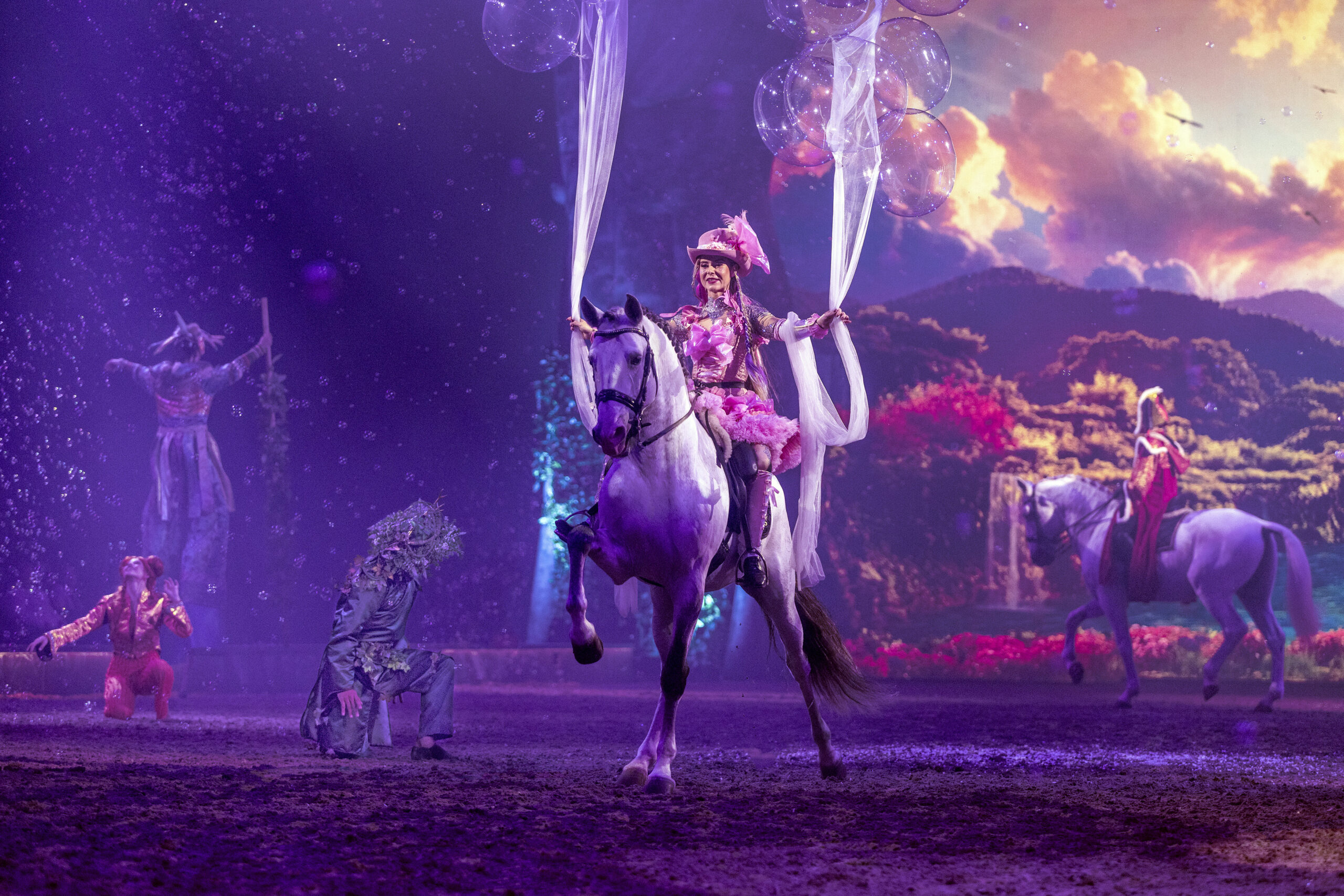 Eine Frau reitet mit ausgestreckten Armen auf einem Schimmel.