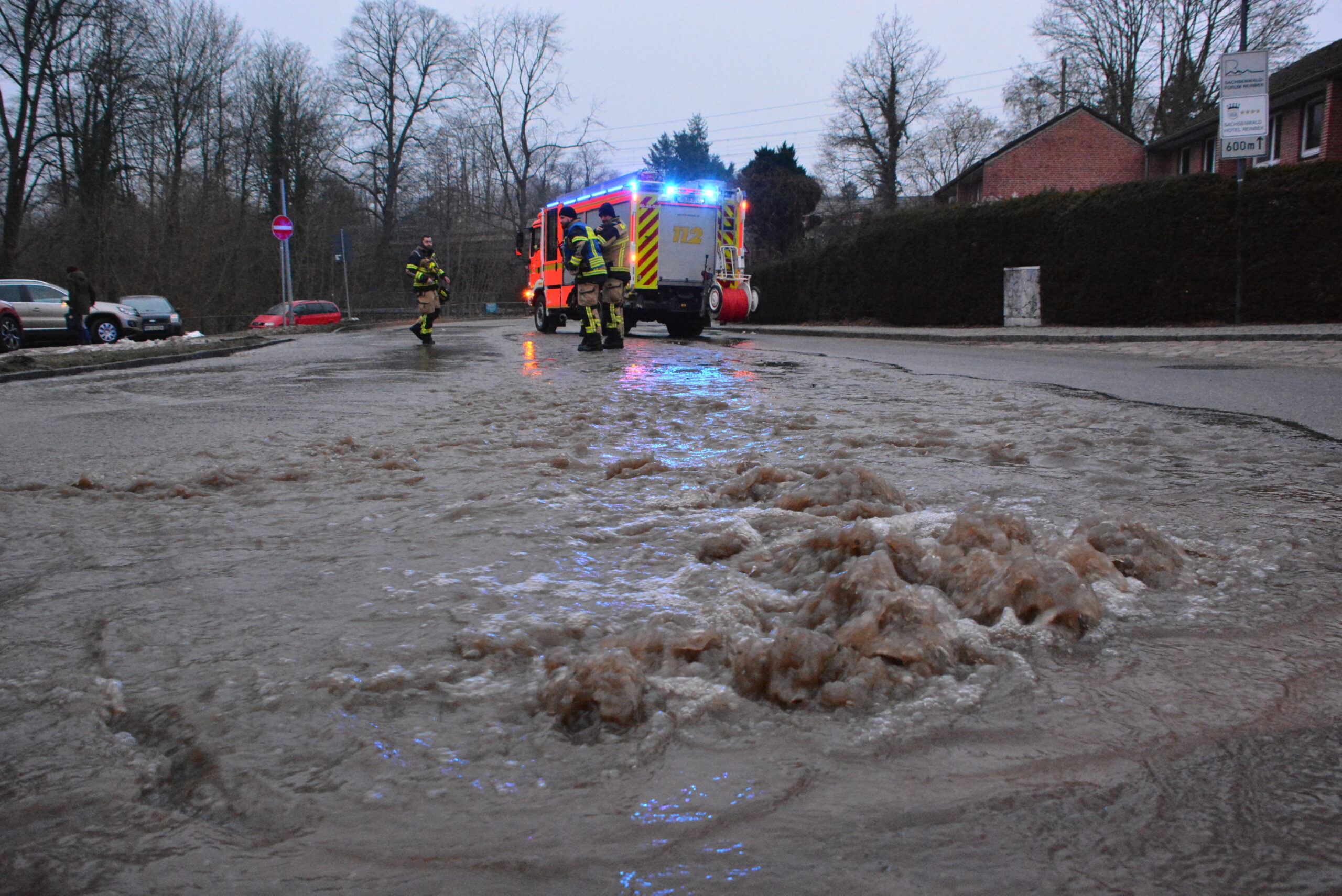 Eine Straße steht unter Wasser. Im Hintergrund sieht man einen Feuerwehrauto.