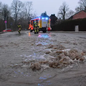 Eine Straße steht unter Wasser. Im Hintergrund sieht man einen Feuerwehrauto.