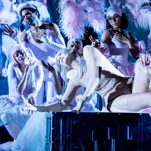 Ein Ensemble an Schauspieler:innen hat sich in Kostümen mit Federn versammelt.