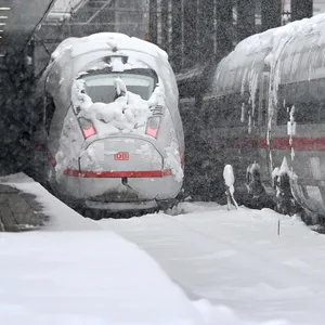 Ein ICE steht auf einem eingeschneiten Gleis am Bahnhof.