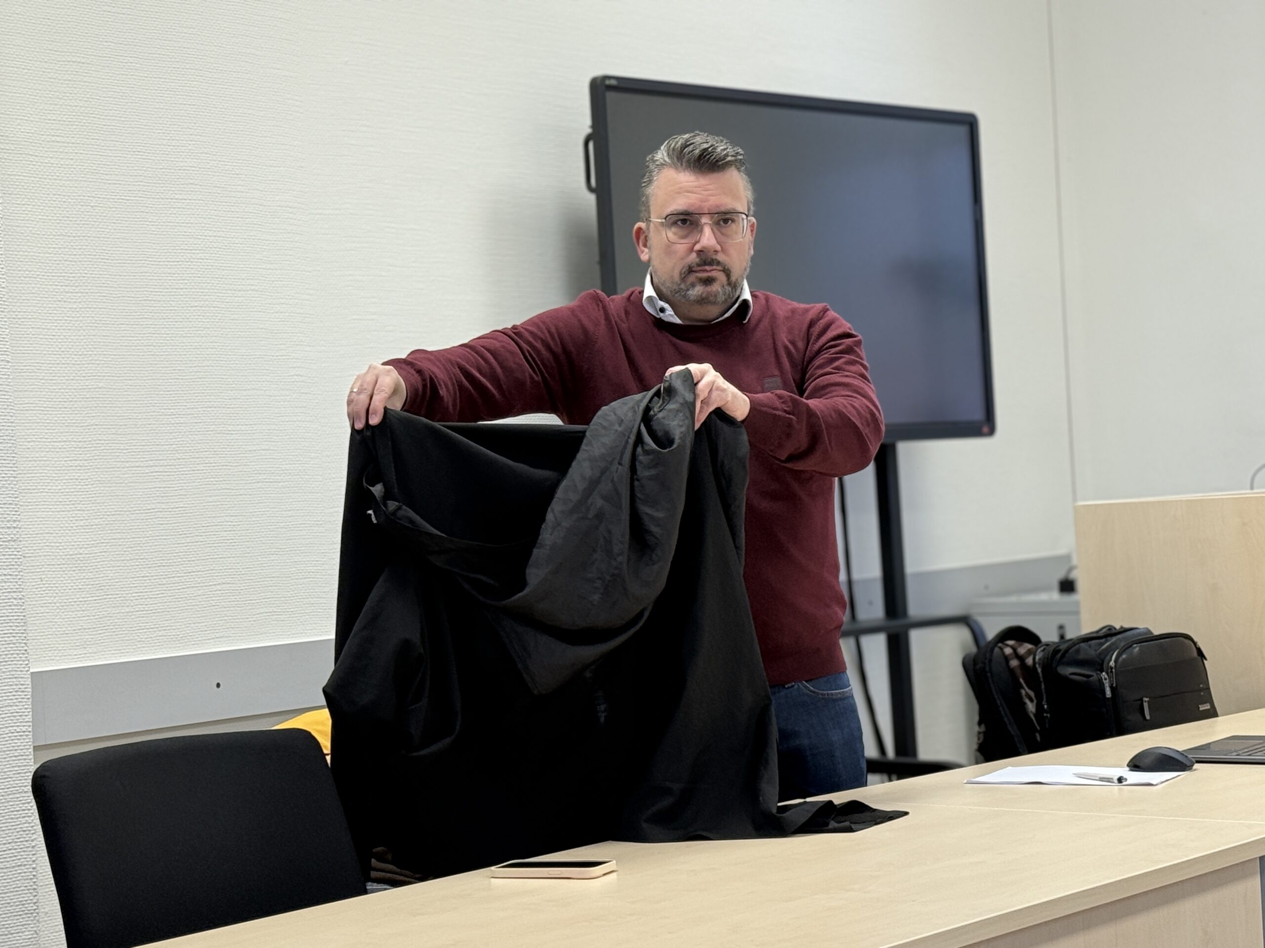 Der Verteidiger von Christa W. hält seine Jacke vor die Angeklagte, sodass man sie nicht sieht.