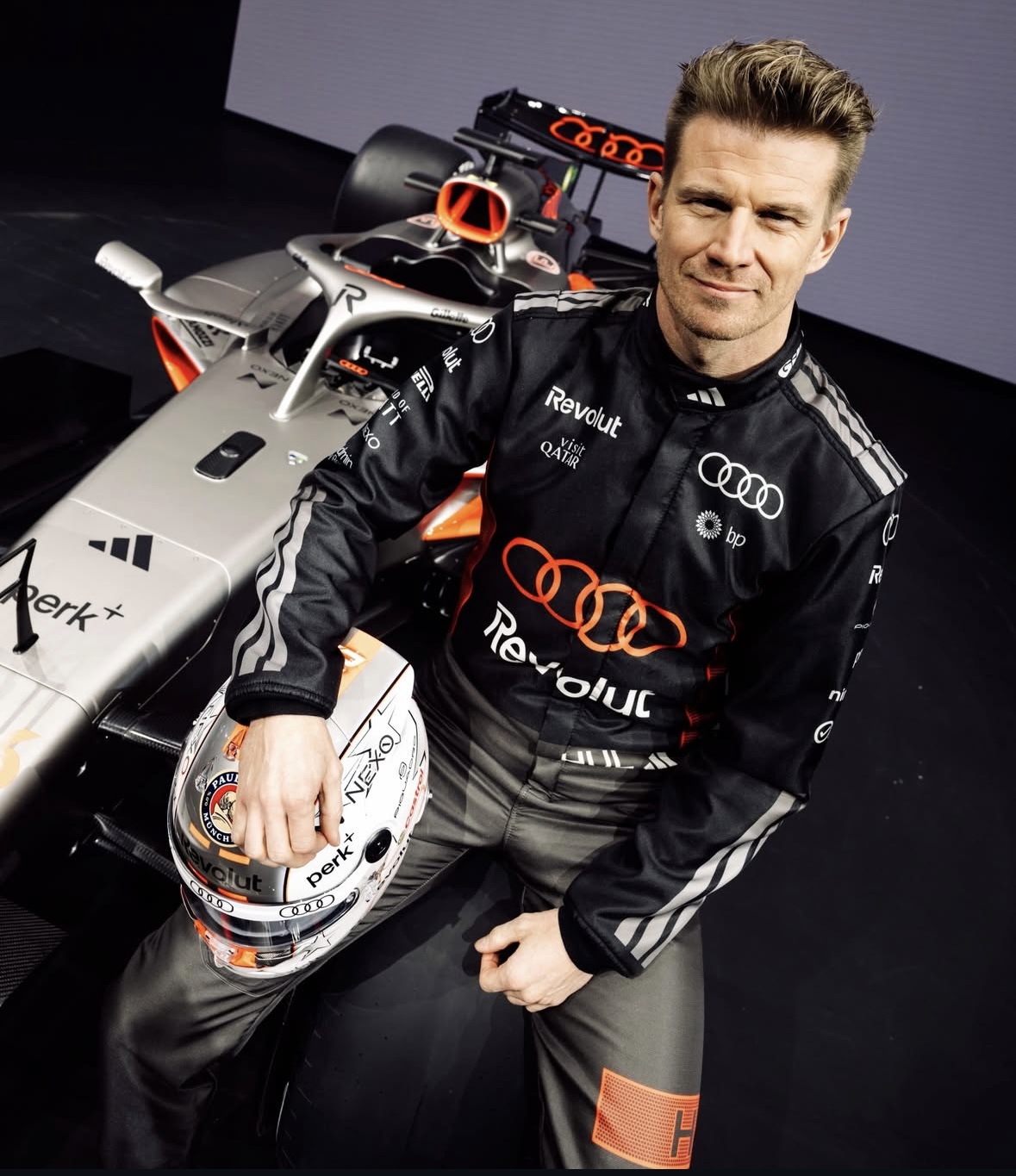 Nico Hülkenberg sitzt mit Helm auf dem Schoß auf seinem Audi-Rennauto.