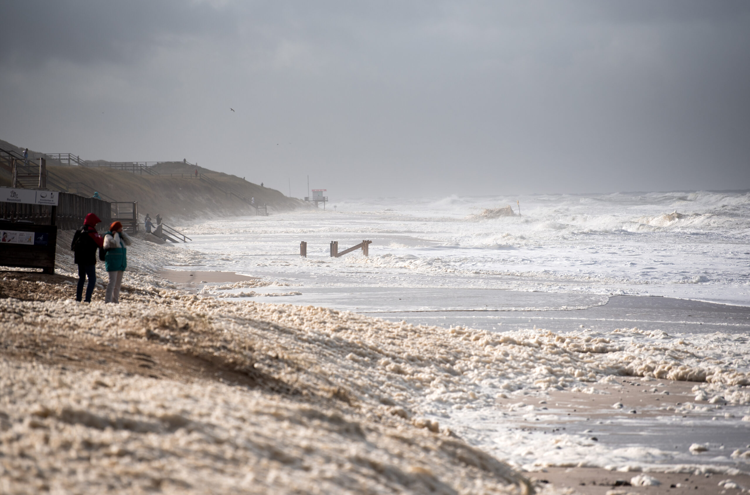 Spaziergänger sind bei einer Sturmflut und Wellen an der Nordsee am Strand von Westerland auf der Nordseeinsel Sylt unterwegs. (Archivbild)