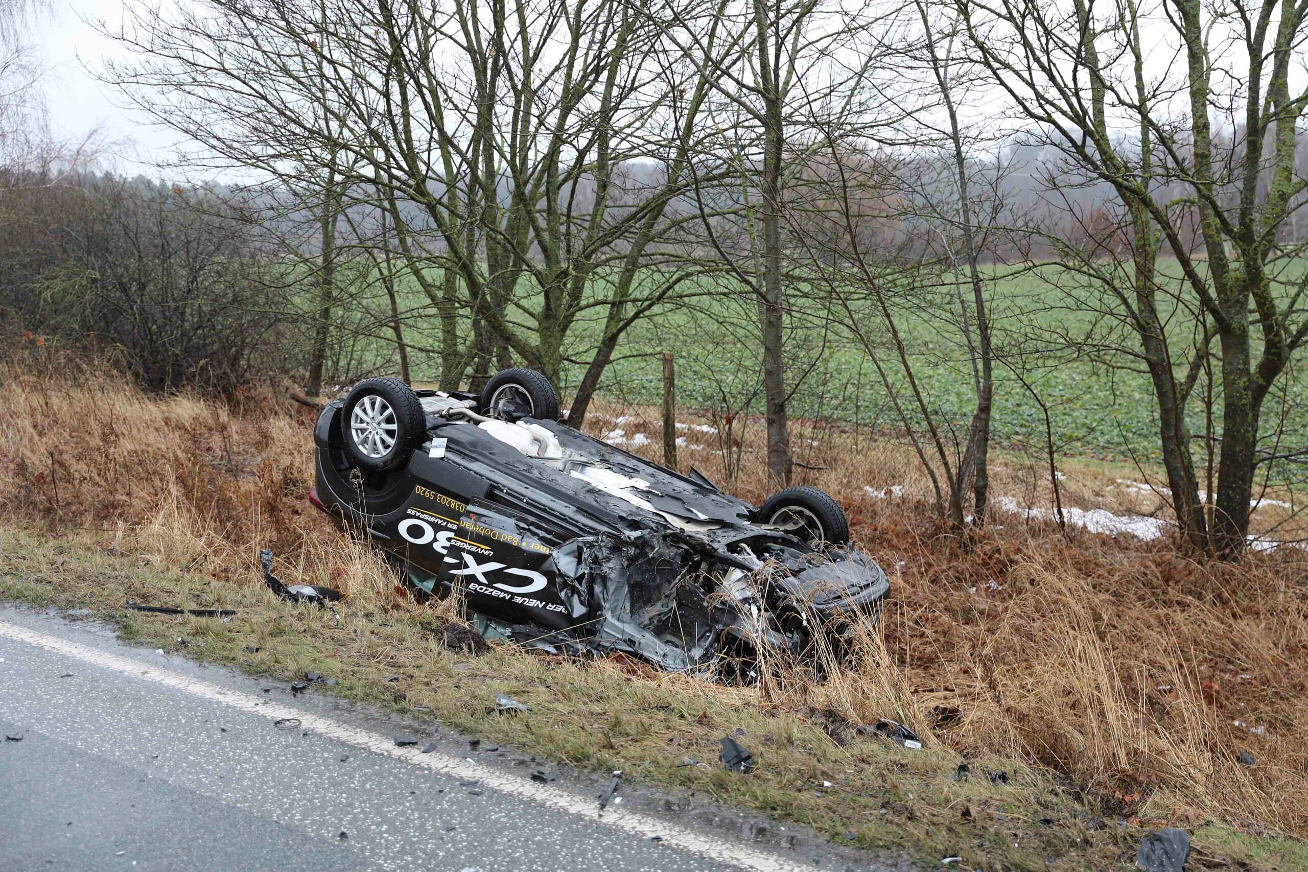 Ein schwarzes Auto liegt kopfüber im Graben.