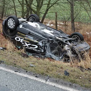 Ein schwarzes Auto liegt kopfüber im Graben.