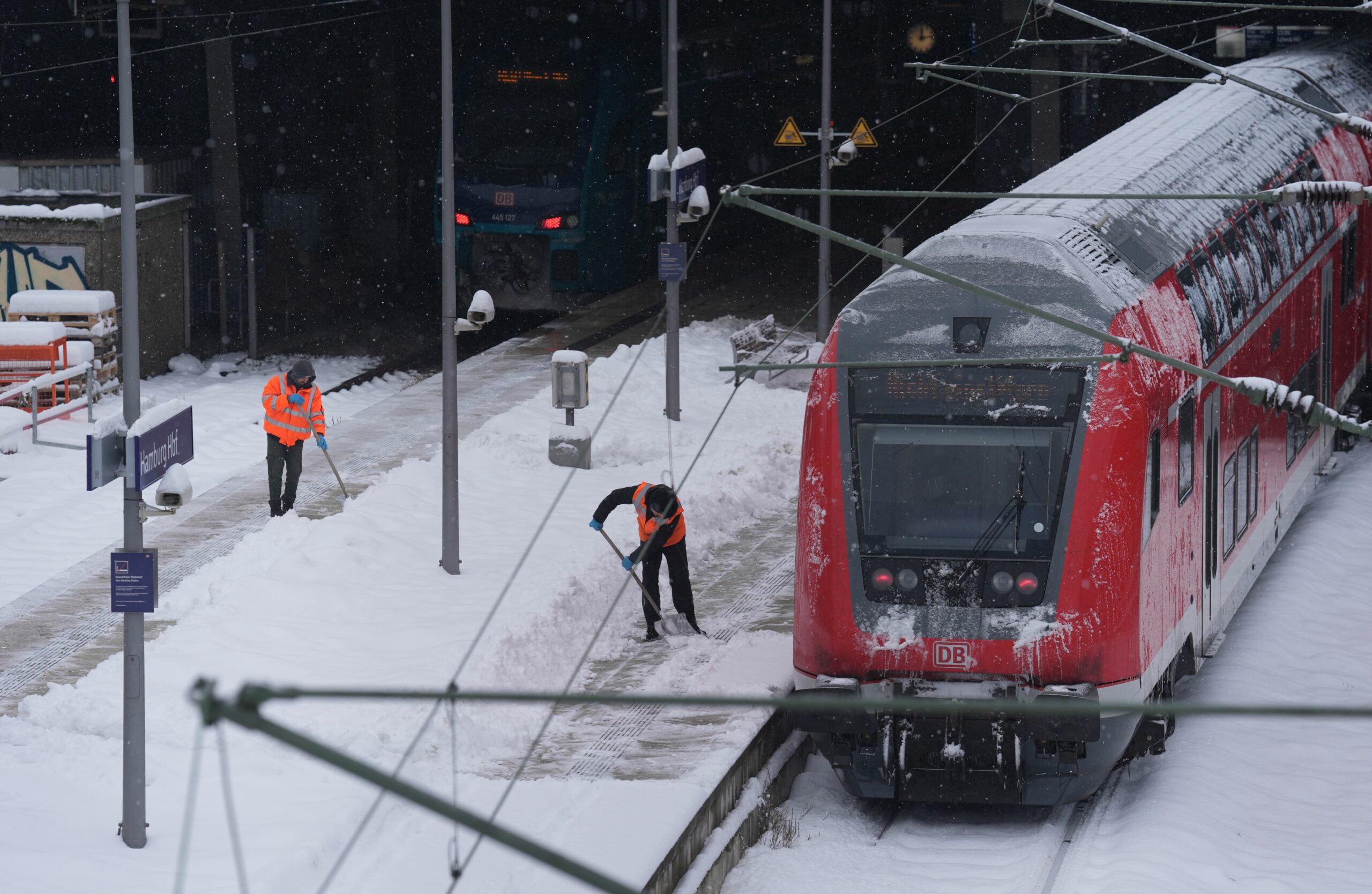 Mitarbeiter beseitigen die zentimeterdicke Schneeschicht auf den Bahnsteigen im Hamburger Hauptbahnhof.