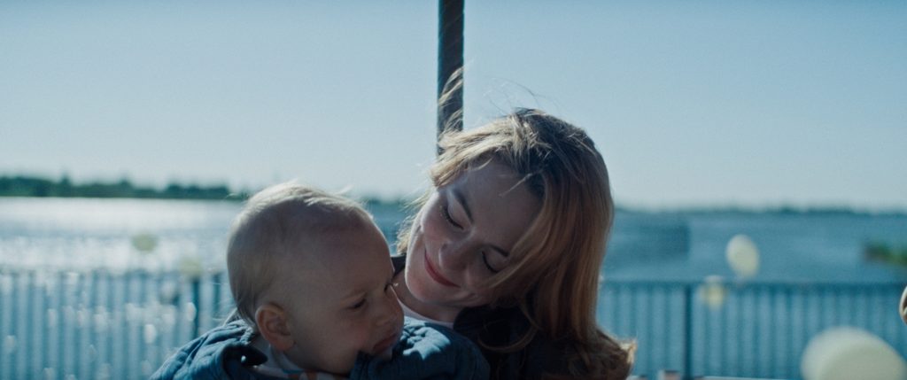 Polizistin Julia (Lea van Acken) mit ihrem Sohn Leon auf einem Karussell am Wasser.