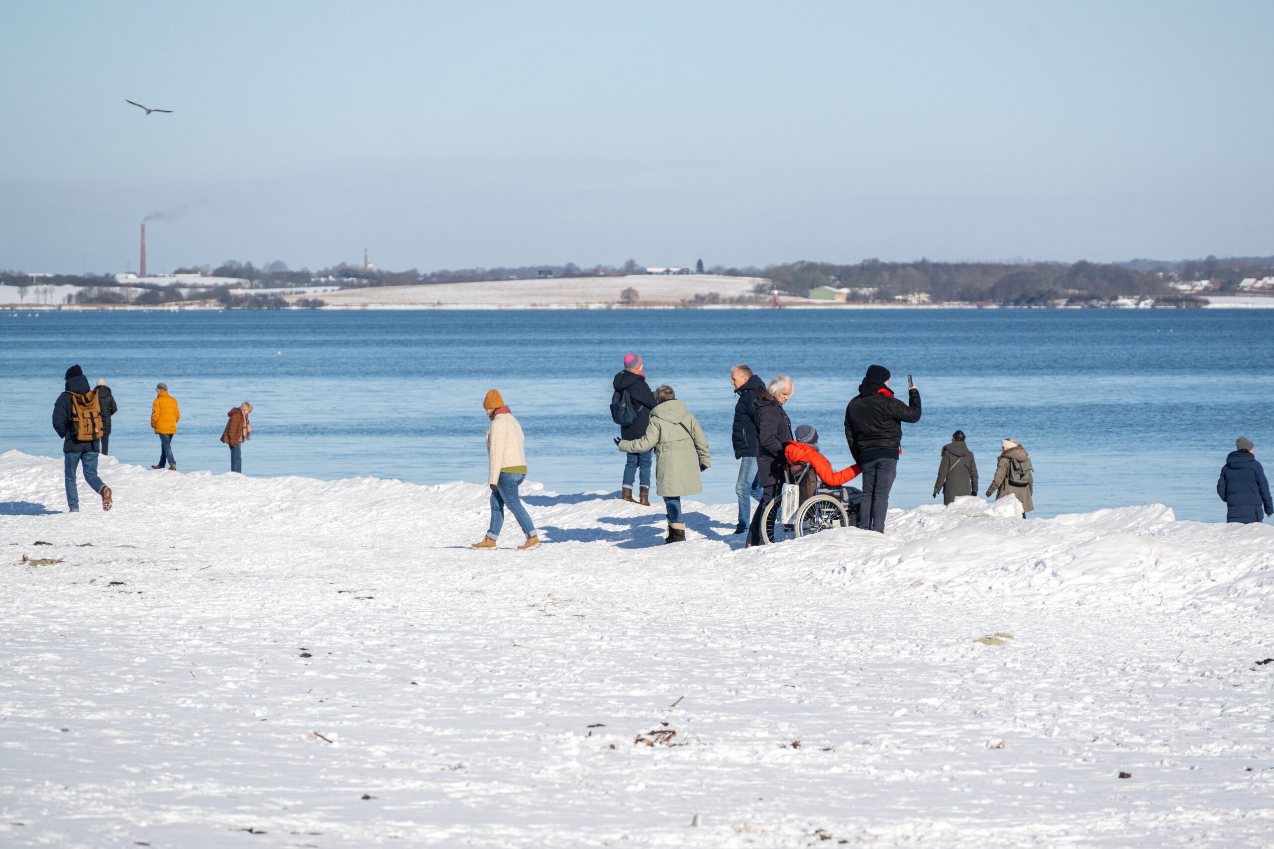 Menschen stehen auf dem Schnee am Strand und machen Fotos.