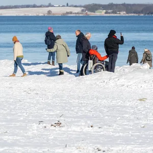 Menschen stehen auf dem Schnee am Strand und machen Fotos.