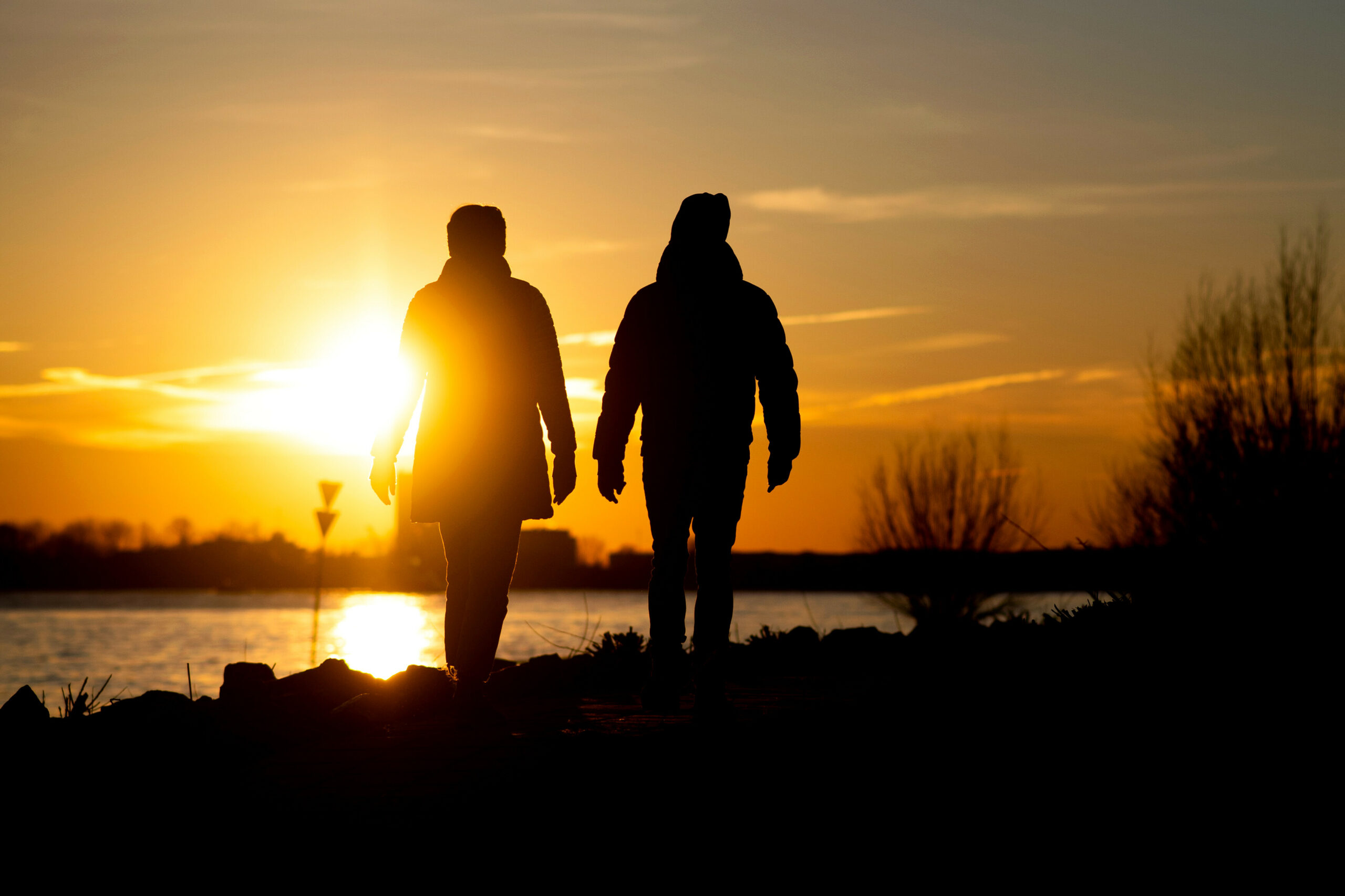 Ein Paar geht vor der untergehenden Sonne am Elbstrand im Hamburger Hafen entlang.