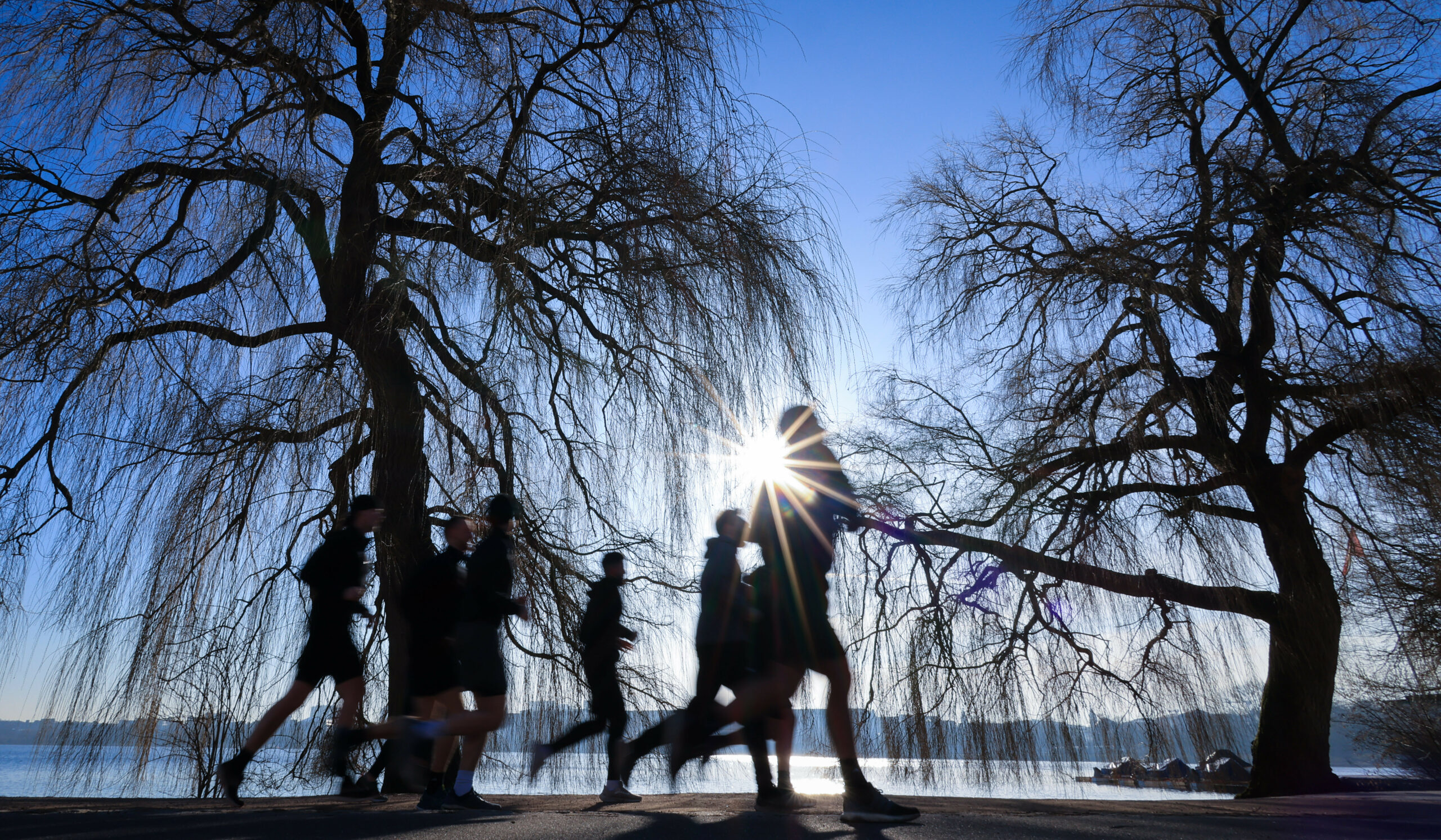 Ein Laufgruppe joggt bei strahlendem Sonnenschein an der Außenalster.