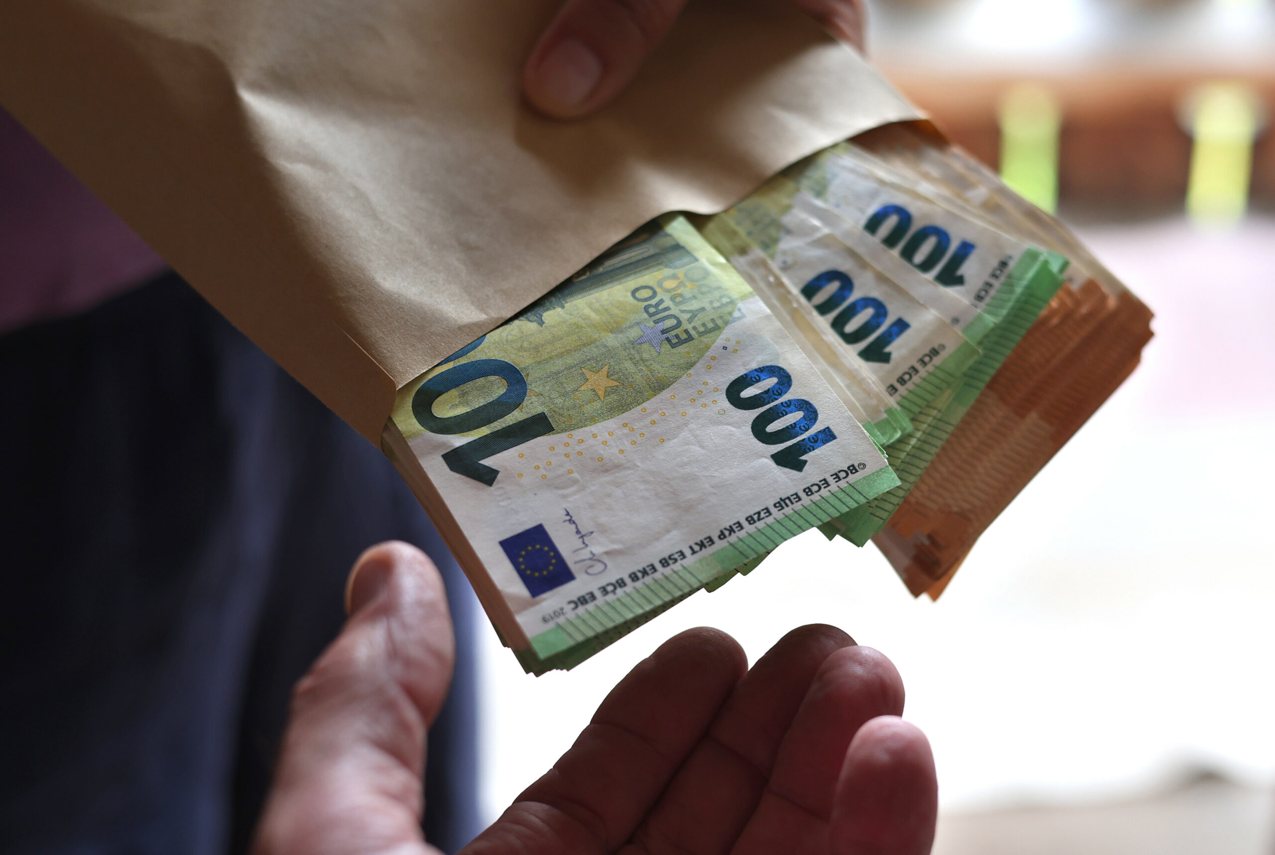 Eine Geldübergabe: Eine Person hält eine Art Brottüte in der mehrere Hunderter und Fünfziger zu sehen sind.