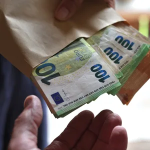 Eine Geldübergabe: Eine Person hält eine Art Brottüte in der mehrere Hunderter und Fünfziger zu sehen sind.