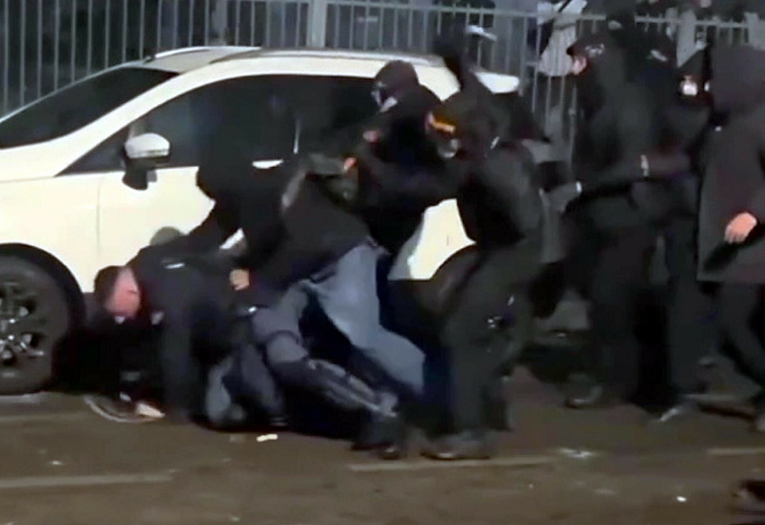 Vermummte Demonstranten attackieren einen am Boden liegenden Polizisten.