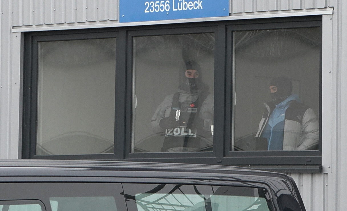 Zollbeamte stehen im durchsuchten Gebäude in Lübeck hinter einem Fenster.