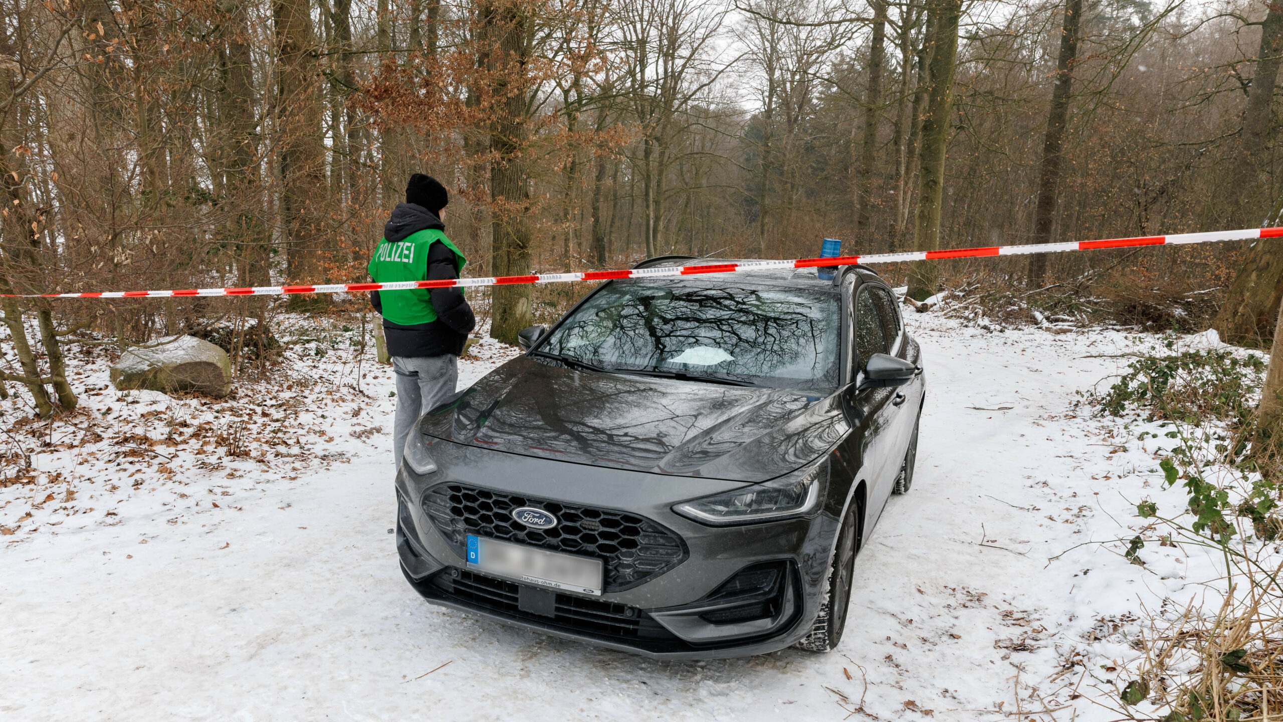 Ein Polizist sperrt die Zufahrt in ein Waldstück. Die Polizei sucht hier nach Spuren eines möglichen Verbrechens.