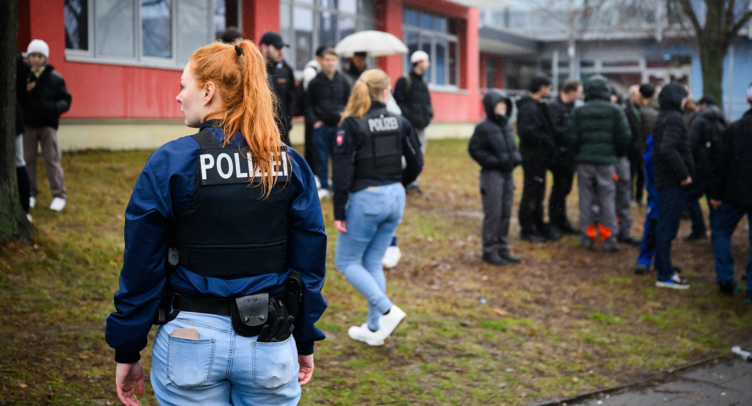 Zwei Polizistinnen stehen inmitten von Schülern vor einer berufsbildenden Schule am Hans-Böckler-Ring.