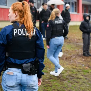 Zwei Polizistinnen stehen inmitten von Schülern vor einer berufsbildenden Schule am Hans-Böckler-Ring.